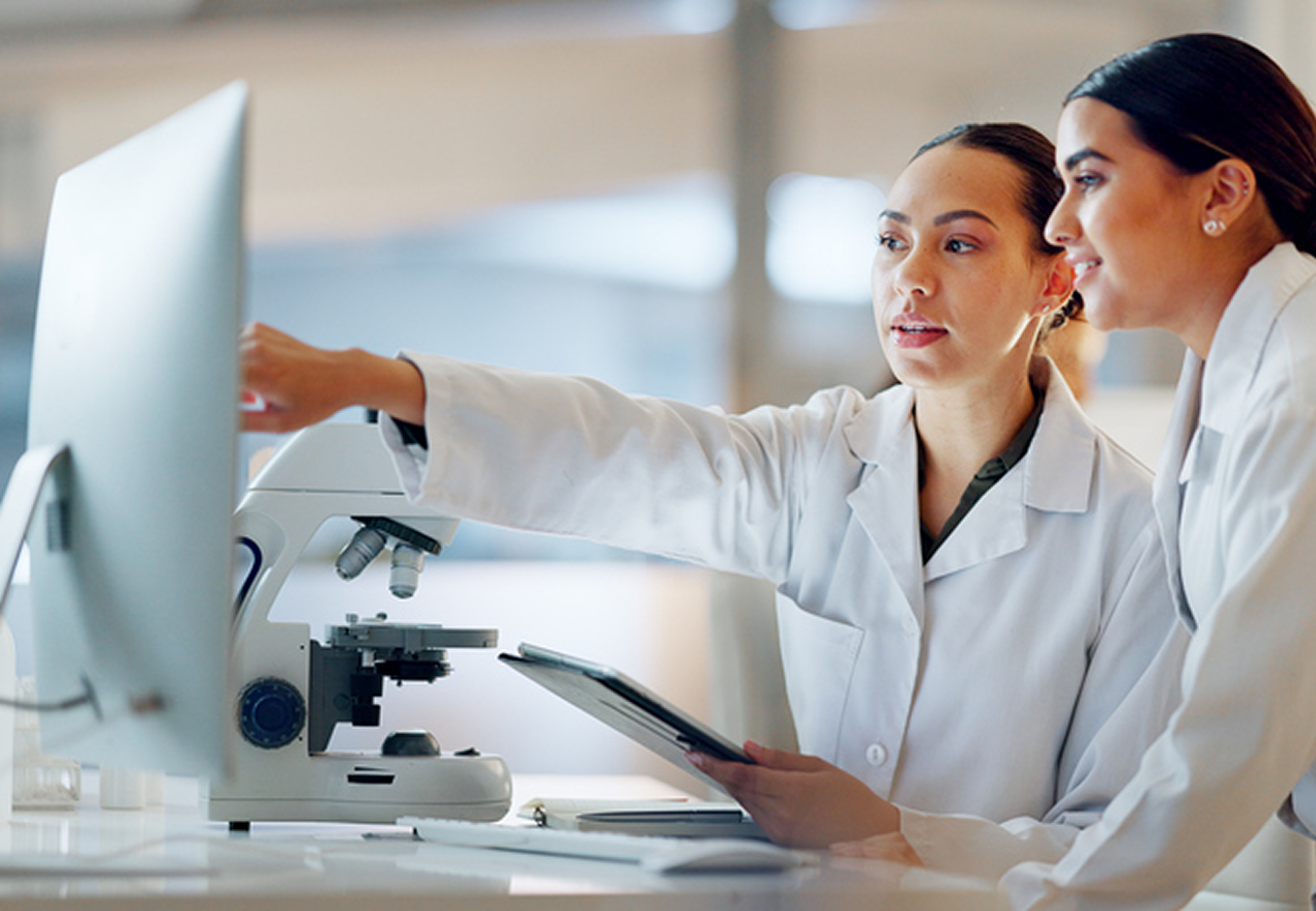 Two women in lab coats pointing at a screen